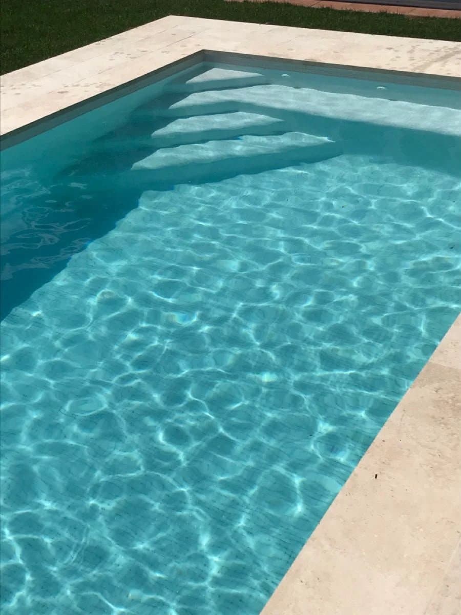 Escalier d'angle intégré et margelles en pierre claire d'une piscine RiverPool
