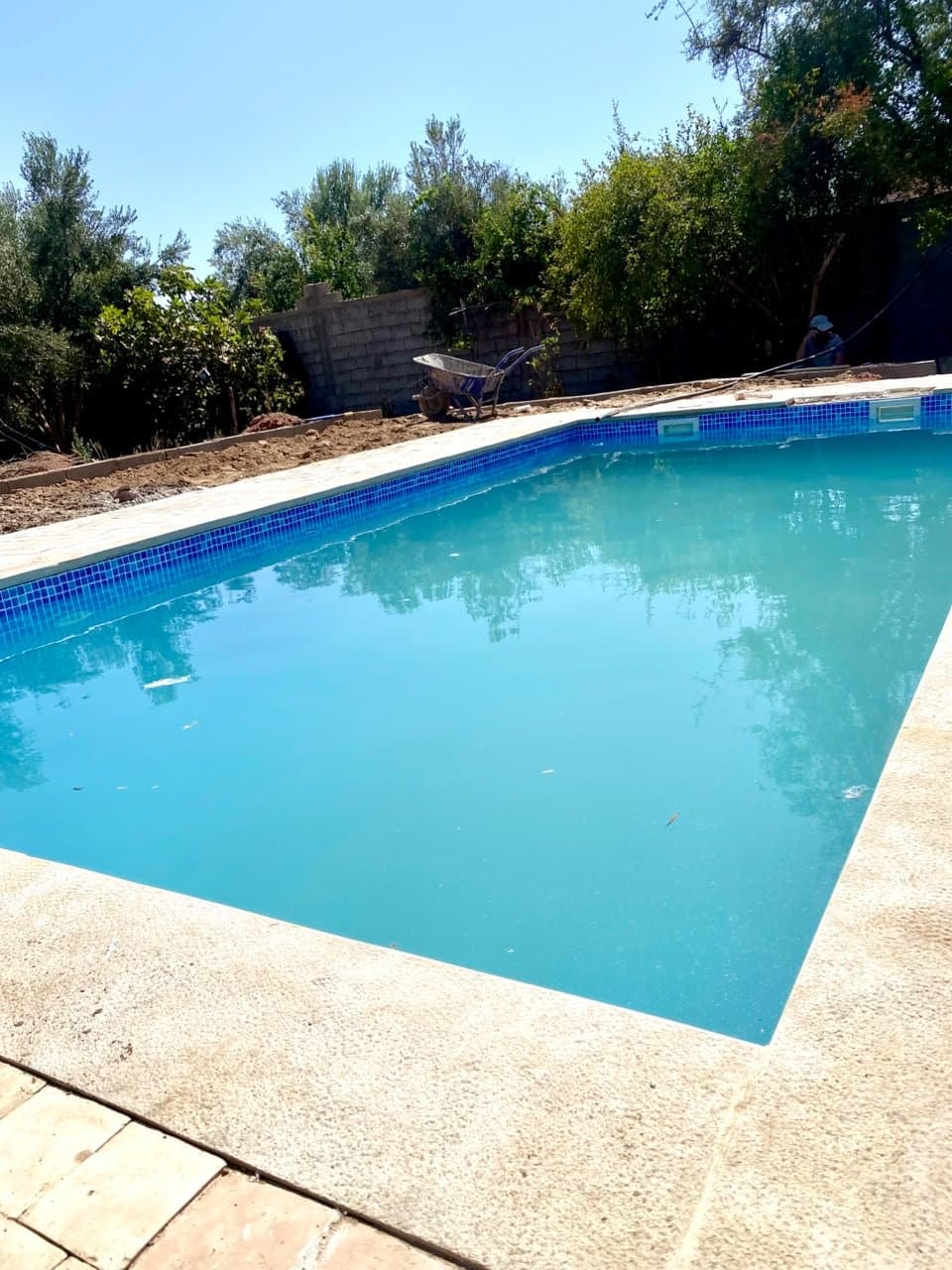 Piscine de jardin RiverPool avec ligne d'eau en mosaïque bleue et margelles en pierre, pendant les finitions