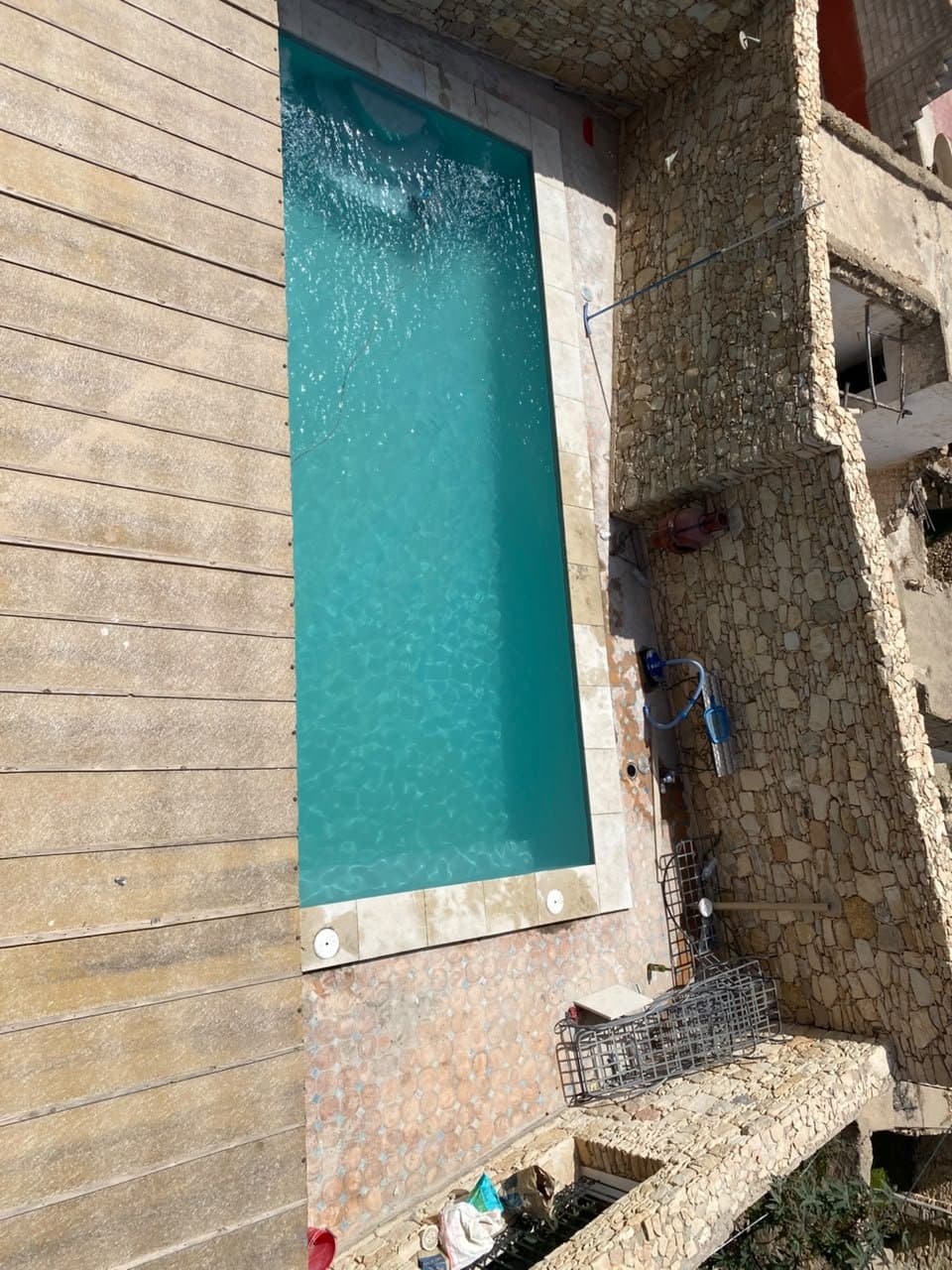 Vue plongeante sur une piscine RiverPool entre terrasse en bois et murs en pierre
